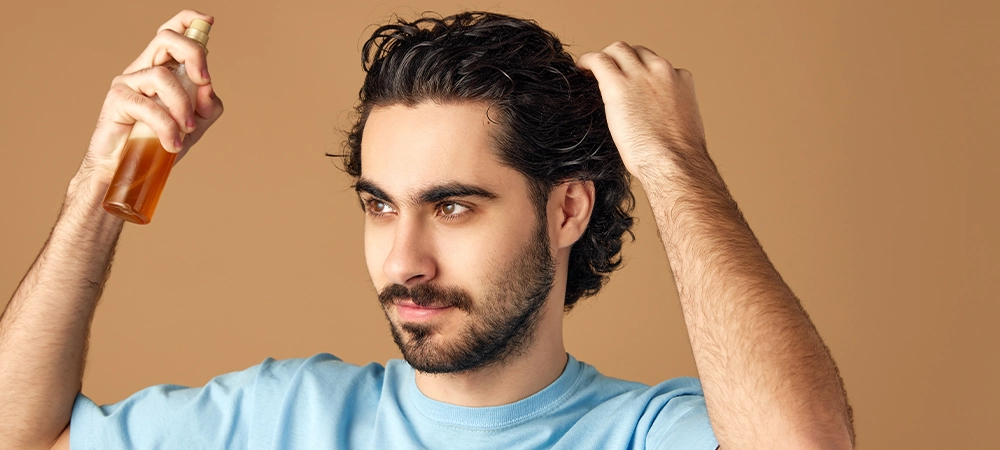 men applying oil spray on his long curly hairs