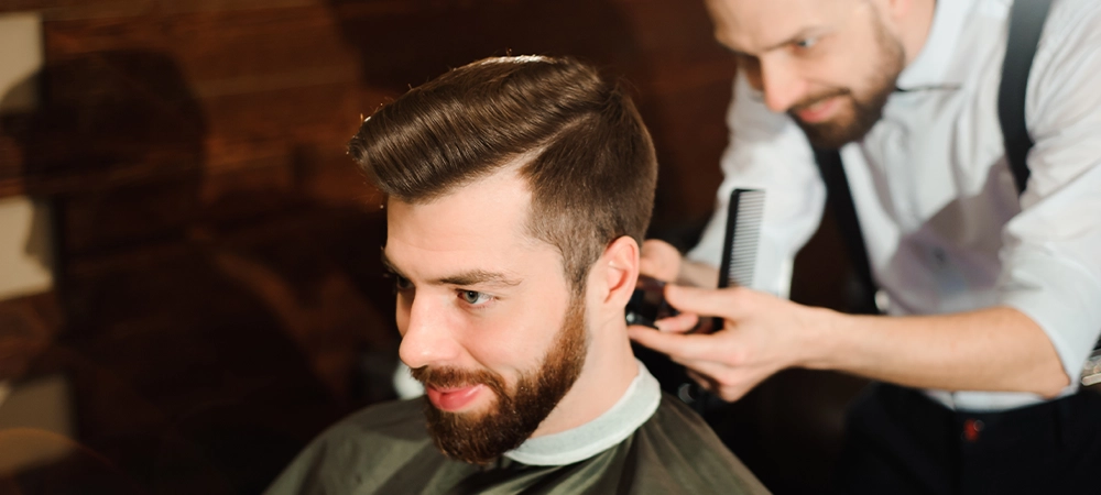 Master cuts hair and beard of men in the barbershop, hairdresser makes hairstyle for a young man