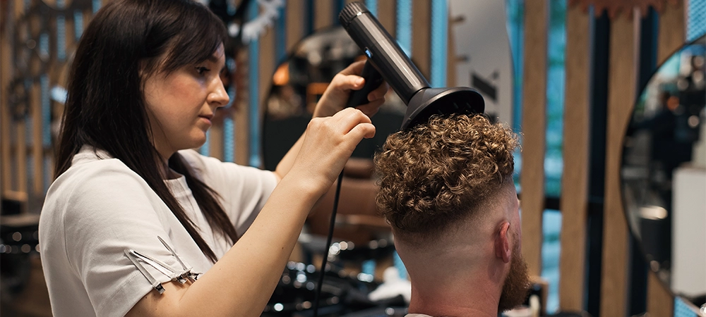 women blow drying the men curly hairs