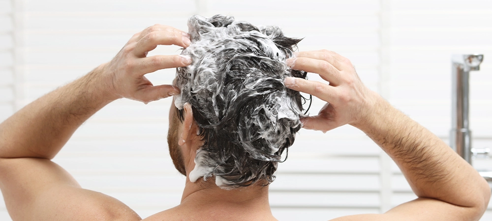 Man washing his hair with shampoo in shower, back view